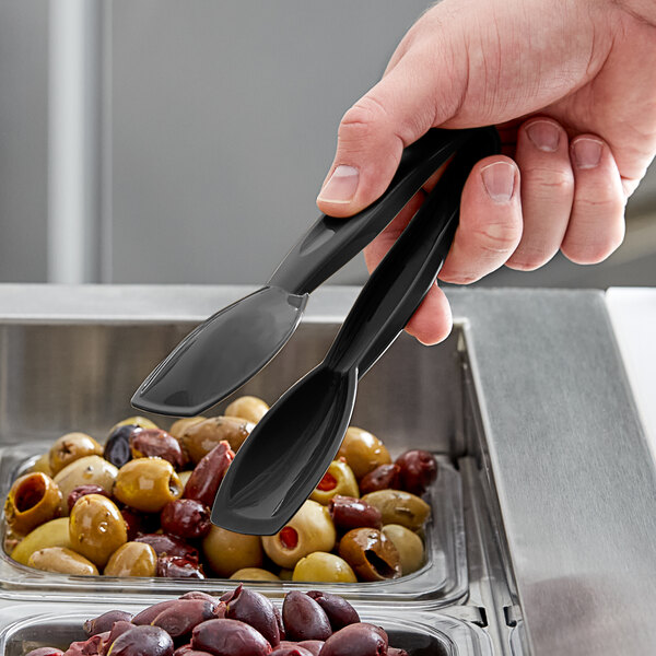 A hand using Cambro black plastic tongs to serve olives.