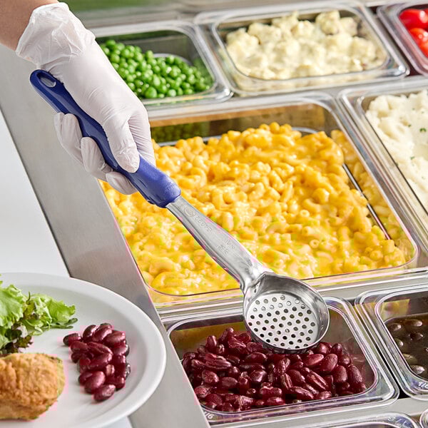 A person wearing gloves uses a Vollrath blue perforated round Spoodle to serve macaroni and cheese from a tray.