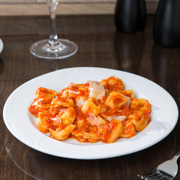 A CAC porcelain plate with pasta and sauce on it on a table with a wine glass.