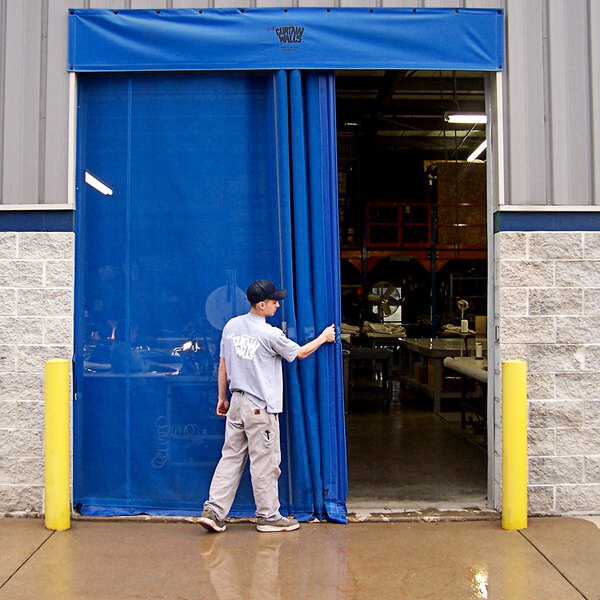 A man in a grey shirt and khaki pants opening a blue mesh curtain.