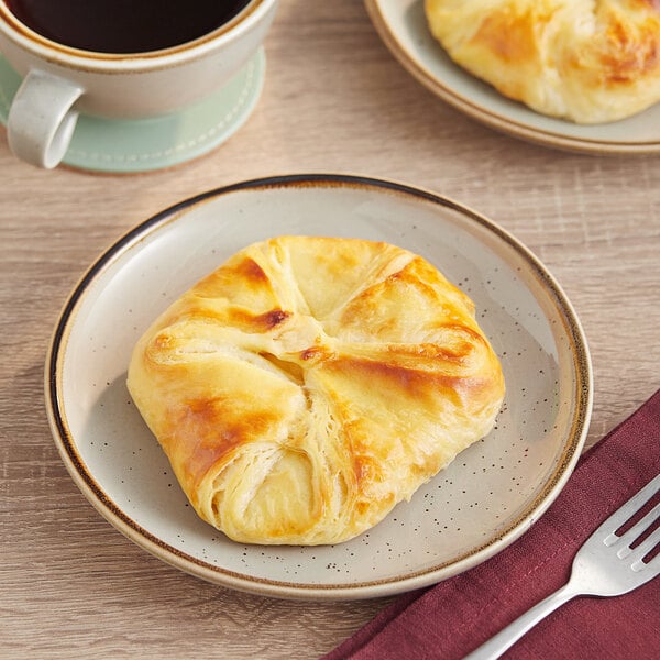 A close up of a plate with a Bridor Ready to Bake Butter Danish and a cup of coffee.