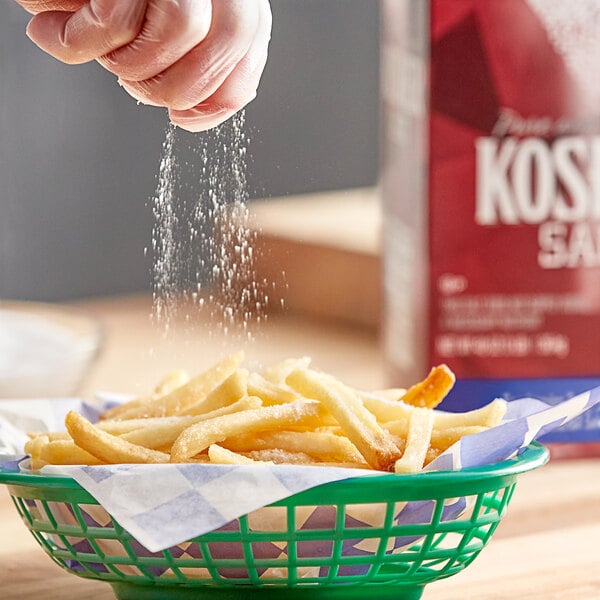 A hand sprinkling Diamond Crystal kosher salt on french fries in a basket.