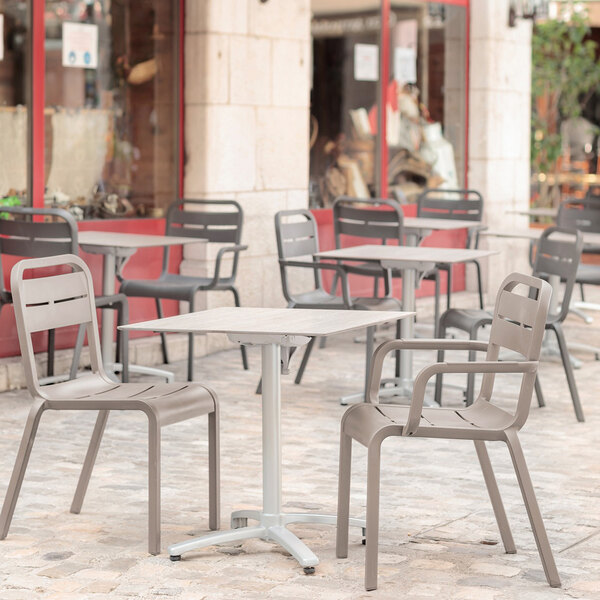 A Grosfillex Cannes French Taupe resin armchair on an outdoor patio with a table.