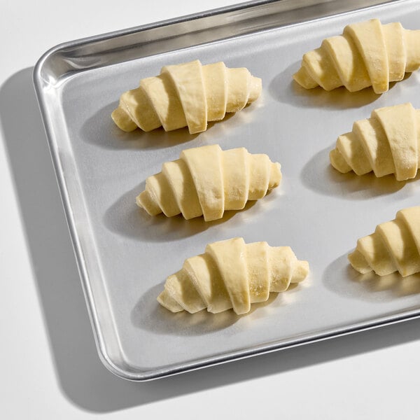 Six unbaked croissants are arranged on a metal baking sheet.