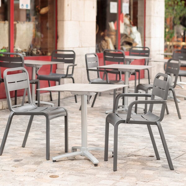 A Grosfillex Cannes charcoal resin outdoor armchair next to a table on a stone patio.