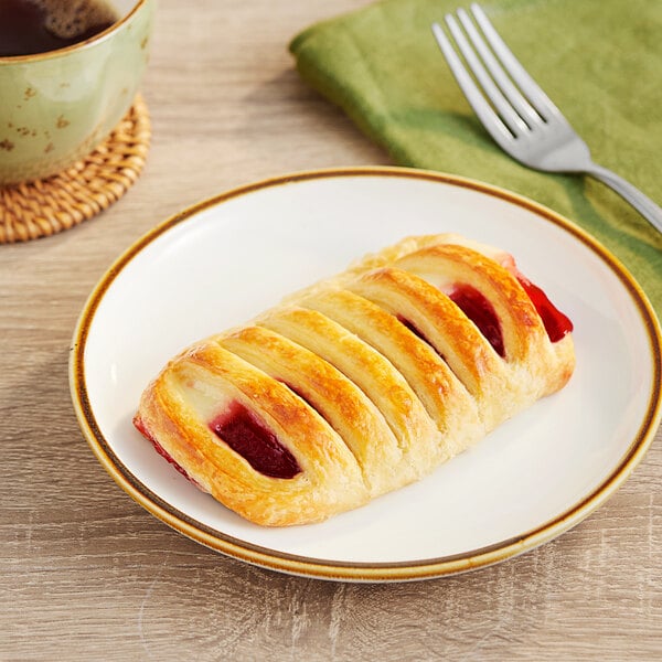 A Bridor cherry Greek yogurt danish on a plate next to a cup of coffee with a fork.