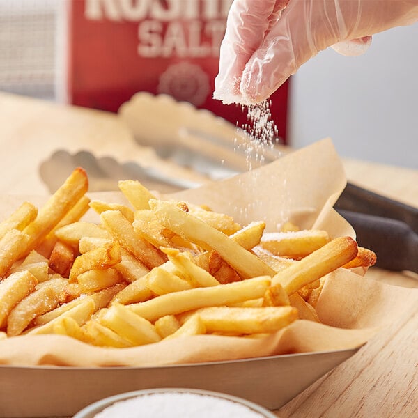 A hand sprinkling Diamond Crystal kosher salt on french fries.
