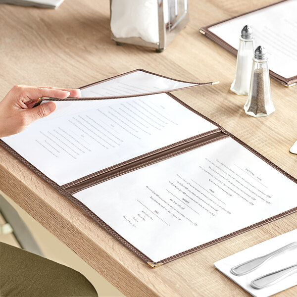 A hand holding a Choice brown trifold menu on a table.