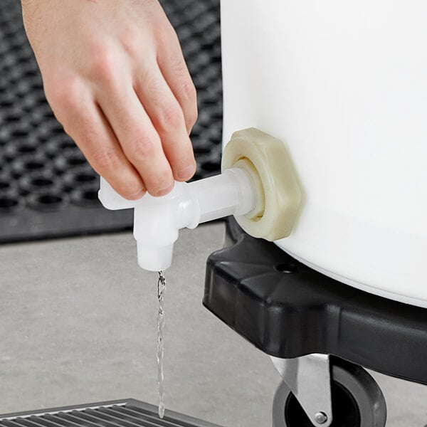 A hand using a white plastic tube to fill a white plastic vegetable crisper bin with liquid.