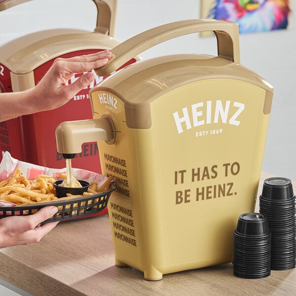 A person pouring french fries into a Heinz countertop mayonnaise dispenser.