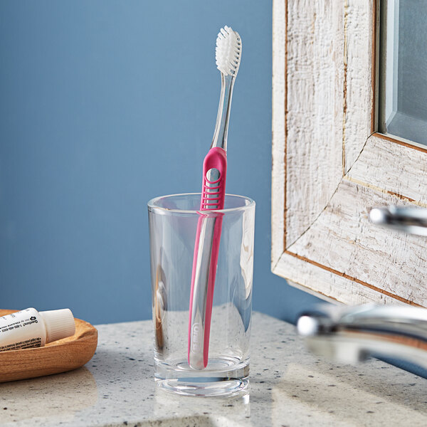 An Oral-B Sensi-Soft toothbrush in a glass on a counter.