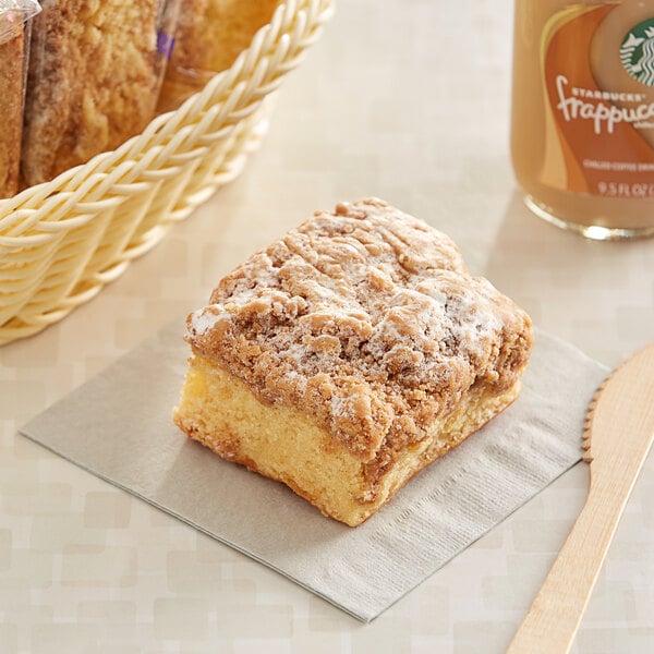 A piece of Sweet Sam's Classic Crumb Cake on a napkin next to a basket of coffee.