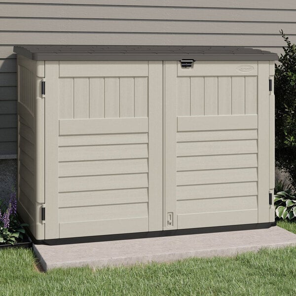 A vanilla Suncast horizontal storage shed with black doors sitting on the grass.