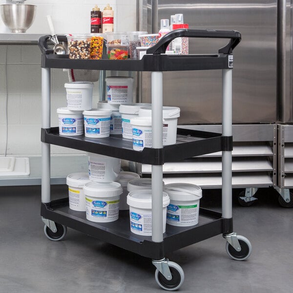 A black Rubbermaid utility cart with three shelves holding food containers.