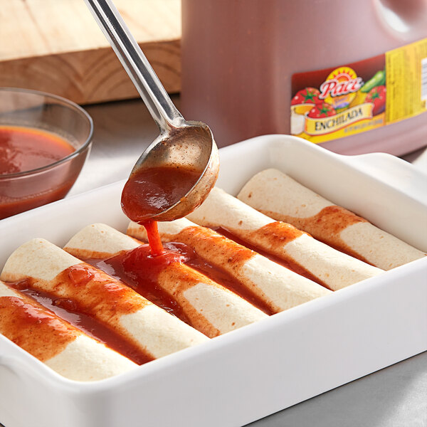 A spoon pouring Pace Enchilada Sauce onto a dish of enchiladas.