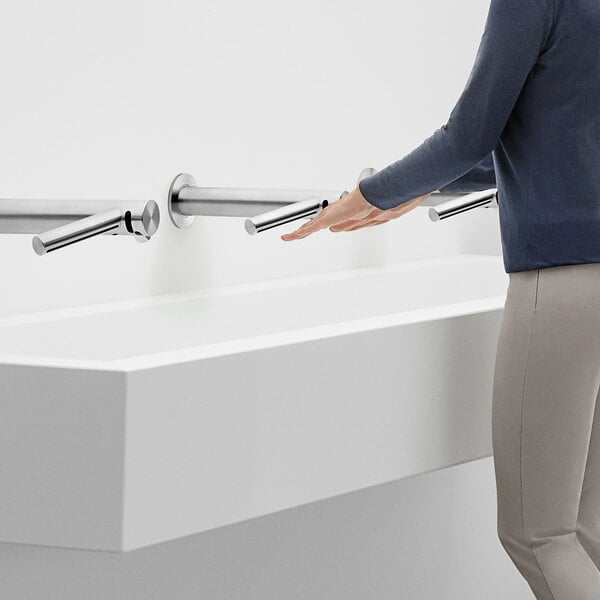 A woman using a Dyson Wash+Dry wall-mounted hand dryer next to a sink.