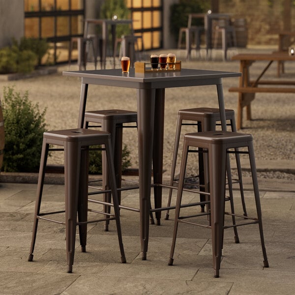 A Lancaster Table & Seating outdoor bar height table with four backless barstools on a patio.