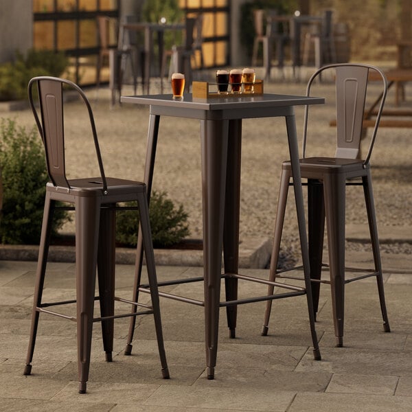 A Lancaster Table & Seating copper bar height table with 2 chairs on an outdoor patio.