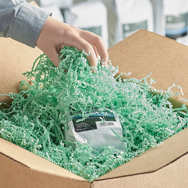 A hand holding a box of Spring-Fill Mint Green Crinkle Cut paper shred.