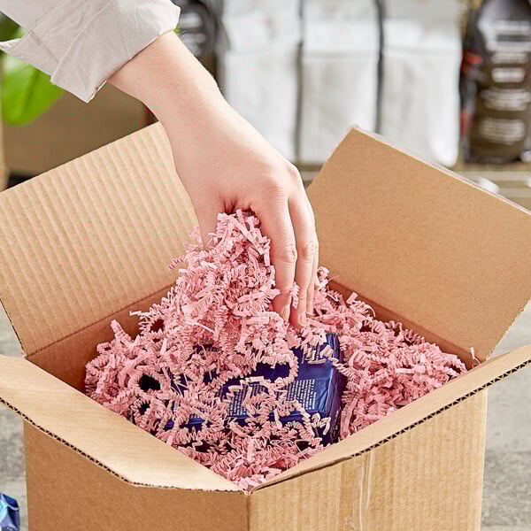 A hand holding a cardboard box with Spring-Fill Light Pink Crinkle Cut paper shred.