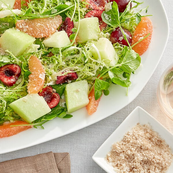 A white square bowl of fruit salad with Maldon Smoked Sea Salt Flakes on top.