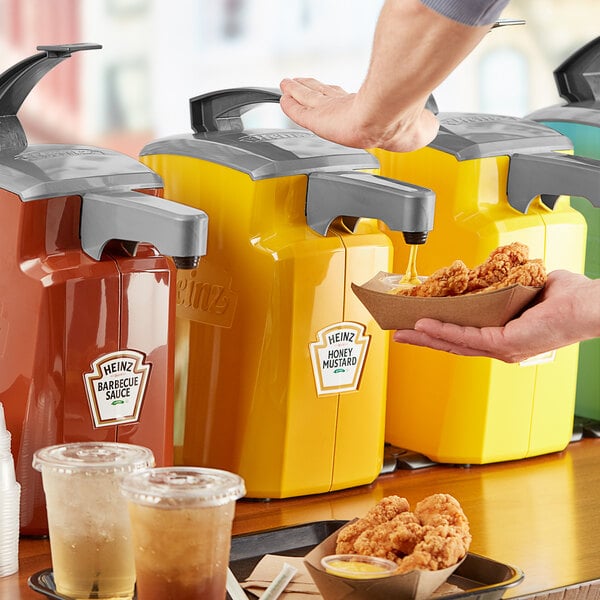 A person pouring Heinz honey mustard from a plastic pump dispenser onto a bowl of fried chicken.