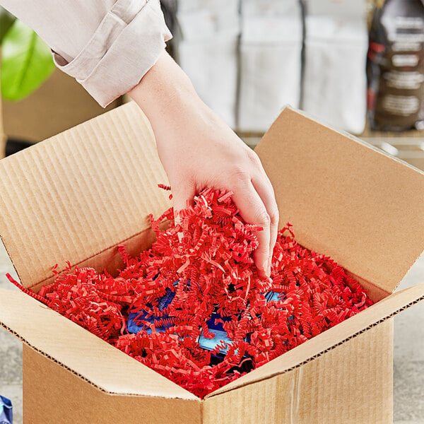 A hand putting Spring-Fill Red Crinkle Cut paper shred into a box.