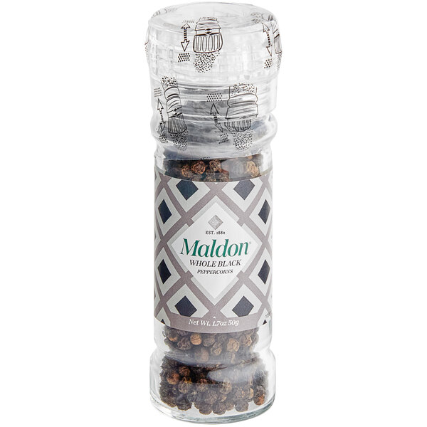 A Maldon black peppercorn grinder on a table with a jar of black peppercorns.