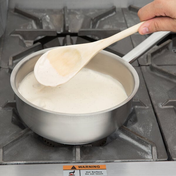 a person holding a wooden spoon over a pot of white liquid