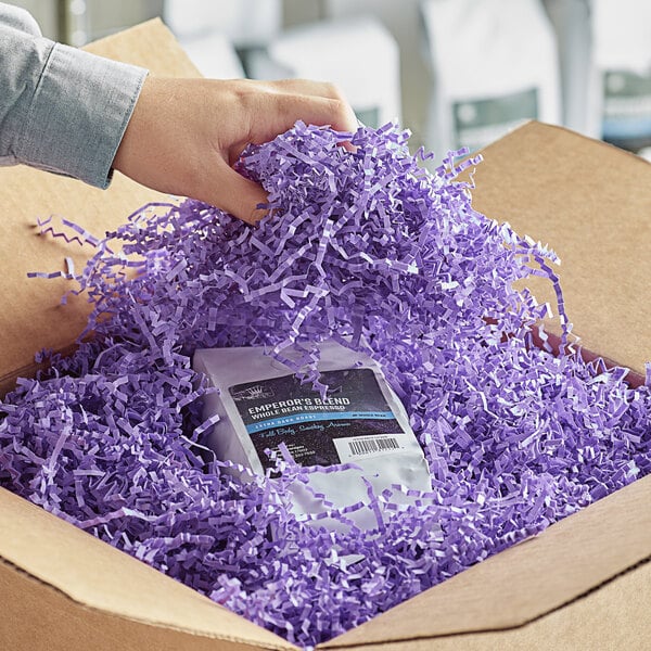 A hand holding a box of Spring-Fill Lavender Crinkle Cut paper shred.