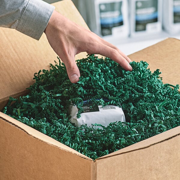 A hand reaching out to a cardboard box filled with Spring-Fill Forest Green Crinkle Cut paper.