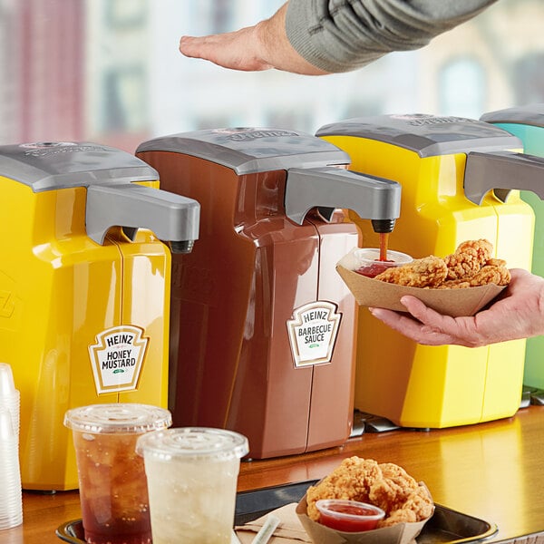 A person using a Heinz plastic barbeque pump to dispense sauce into a bowl of chicken.