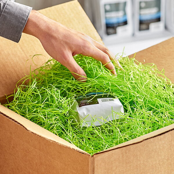 A hand using Spring-Fill Lime Green Very Fine Paper Shred to pack a box.