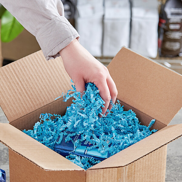 A hand holding Spring-Fill light blue crinkle cut paper shred over a cardboard box.