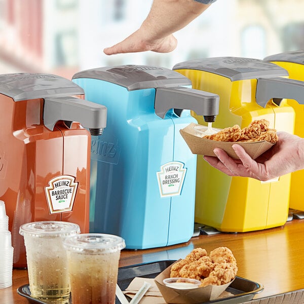 A person using a Heinz blue countertop pump to dispense ranch dressing into a bowl of food.