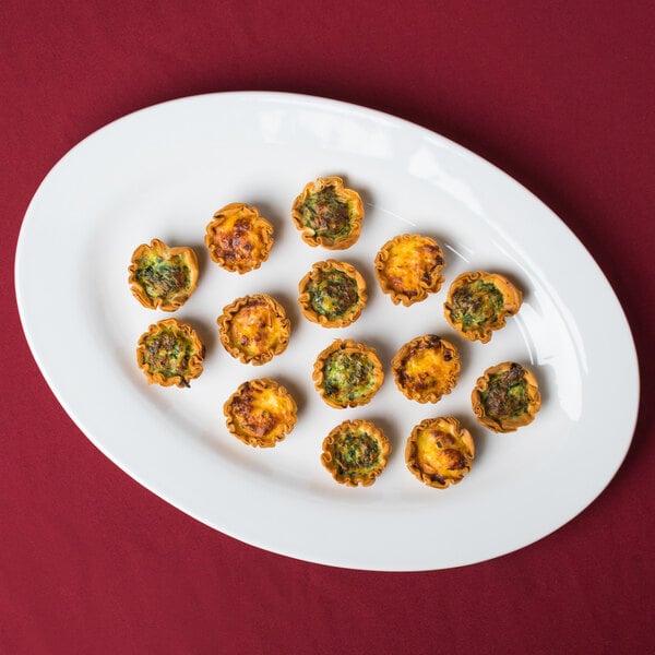 A Tuxton Alaska china platter with mini cheese and pepper tarts on a red surface.