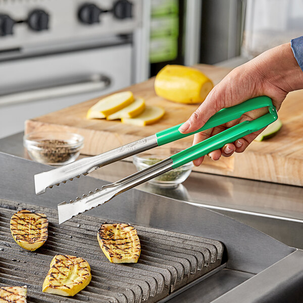 A person using Vollrath VersaGrip tongs with green Kool-Touch handles to grill yellow squash.