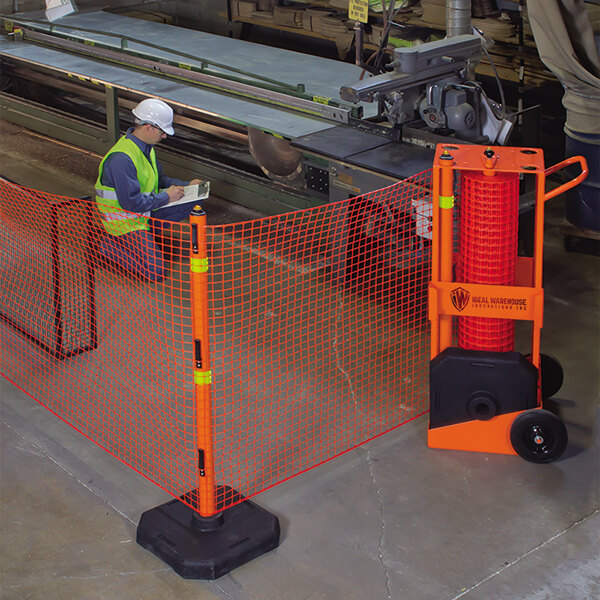 An Ideal Warehouse portable safety zone barrier system with orange netting set up by a man in a safety vest and white helmet.
