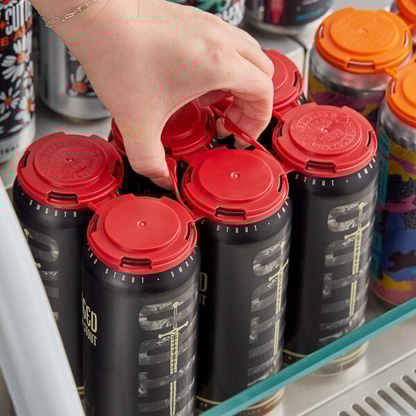 A hand using a red PakTech can carrier to open a black beverage can.