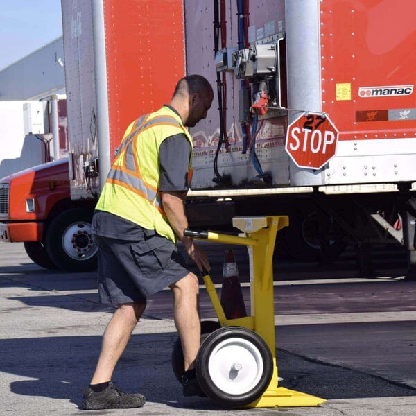 A man in a safety vest using an Ideal Warehouse AutoStand Plus Trailer Stand to push a yellow cart.
