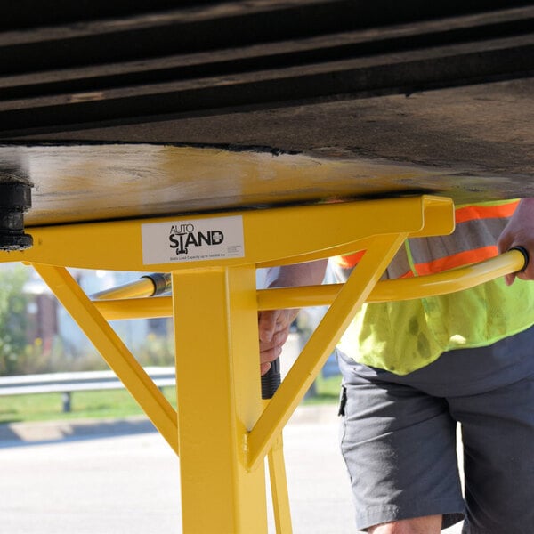 A person using an Ideal Warehouse AutoStand Plus trailer stand, a yellow bar with a black hook on the end.