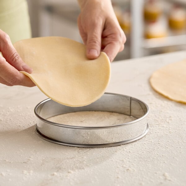 A round stainless steel deep tart ring being used to shape pastry dough.