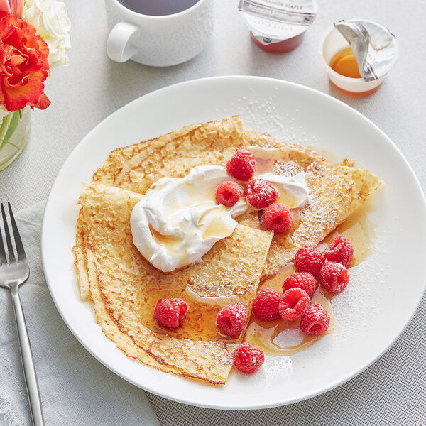 A plate of crepes with raspberries and Runamok Bourbon Barrel-Aged Maple Syrup served in a white cup.
