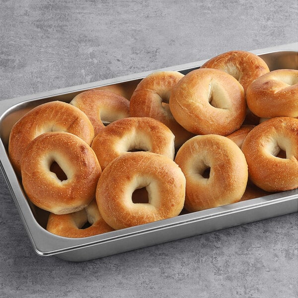 A metal pan filled with Original Bagel New York Style Plain Bagels on a table.