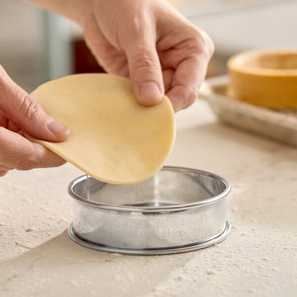 A round stainless steel deep tart ring with rolled edges being used to shape dough.