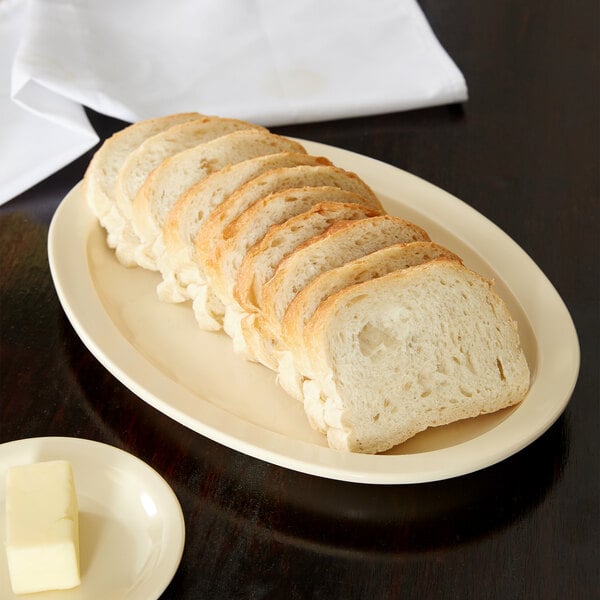 A Carlisle tan oval platter with sliced bread and butter on it.