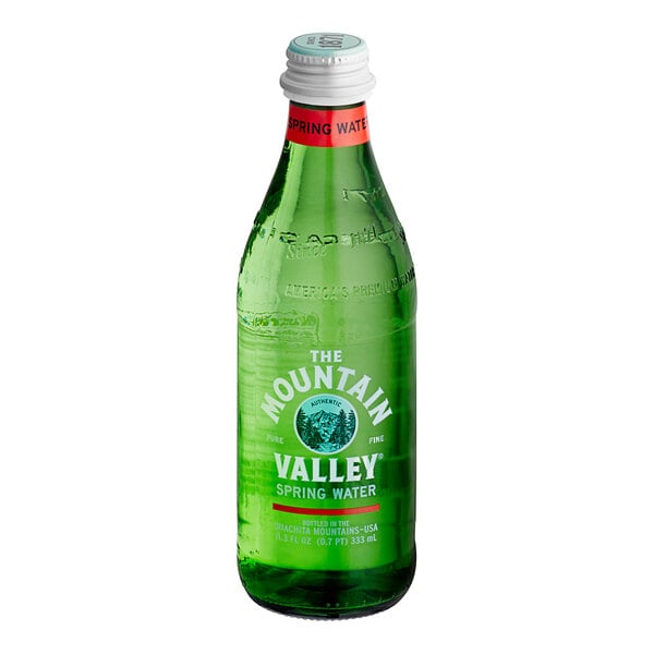 A green glass bottle with a white cap and red neck label, featuring white text that reads 'The Mountain Valley Spring Water.'