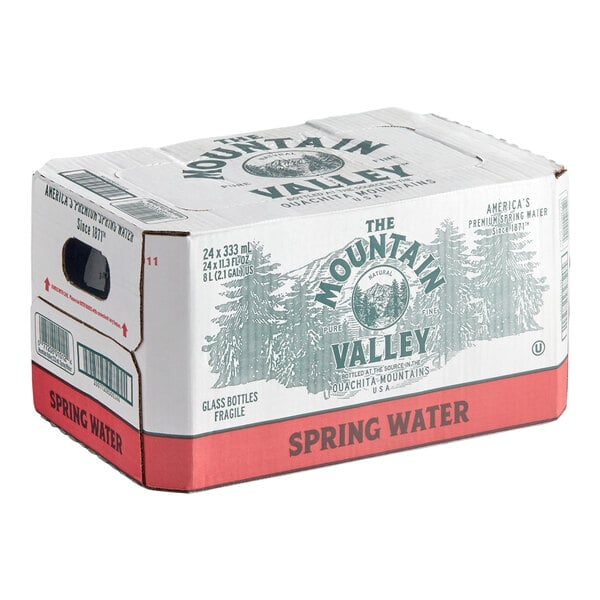 A cardboard box labeled 'Mountain Valley Spring Water' with graphics of trees and text indicating it contains 24 glass bottles of spring water.