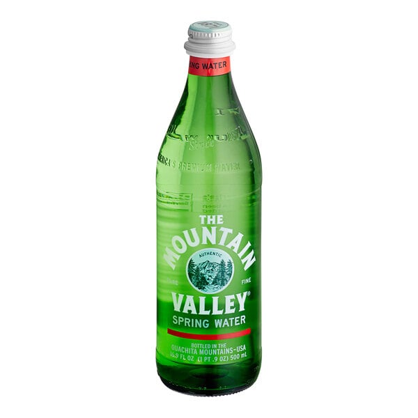 A green glass bottle with a white cap and red neck label, featuring white and green text that reads 'The Mountain Valley Spring Water.'