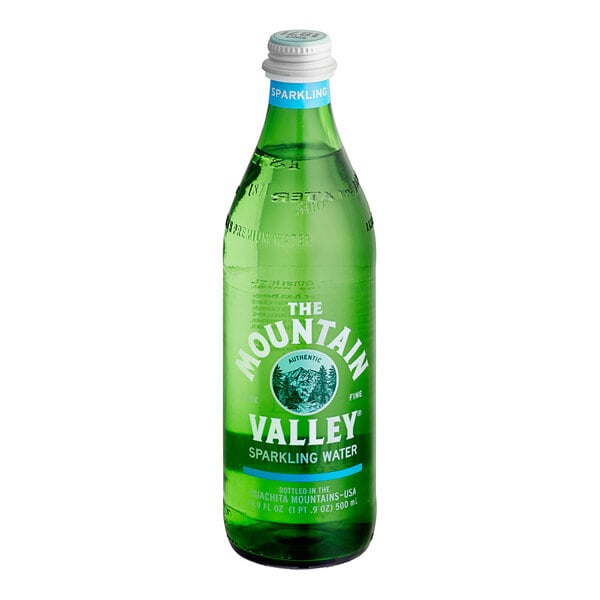 A green glass bottle with a white cap and blue neck label, featuring white text that reads 'The Mountain Valley Sparkling Water.'